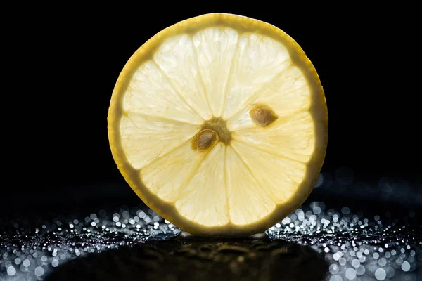 Slice of lemon on black background with water drops and backlit — Stock Photo