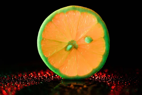 Slice of neon lemon with bokeh on black background — Stock Photo