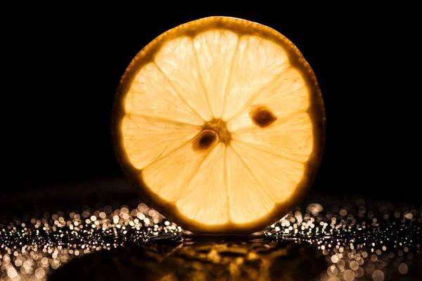 Tranche de citron frais sur fond noir avec rétroéclairage jaune — Photo de stock