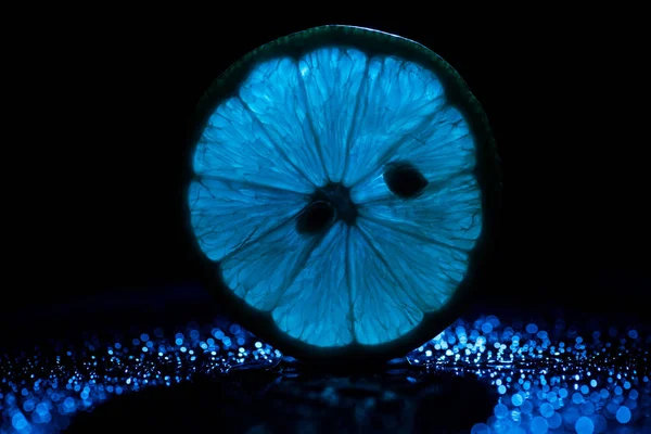 Tranche de citron sur fond noir avec rétroéclairage bleu — Photo de stock