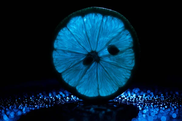 Slice of lemon on black background with blue backlit — Stock Photo