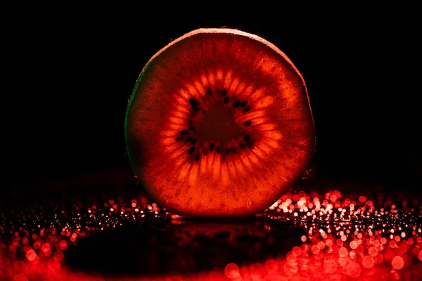 Slice of kiwi on black background with neon red backlit — Stock Photo