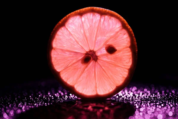 Slice of lemon on black background with red backlit — Stock Photo