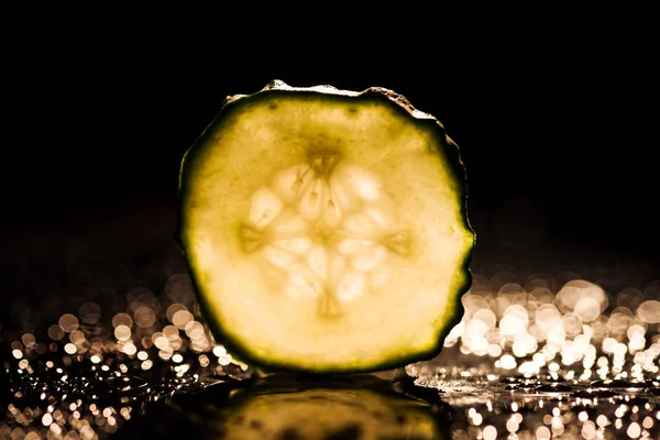 Slice of cucumber with yellow back light on black background — Stock Photo