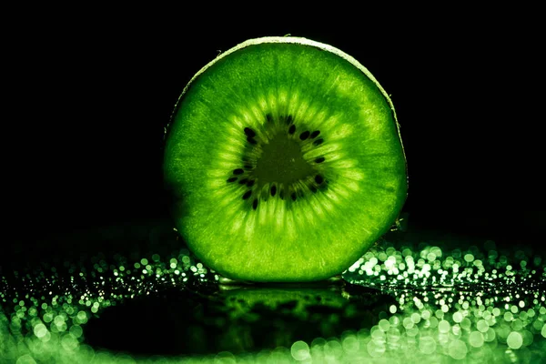Slice of kiwi fruit on black background with neon green backlit — Stock Photo