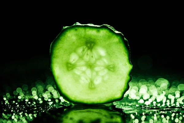 Slice of cucumber with green back light on black background — Stock Photo