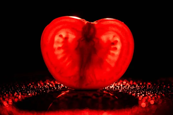 Slice of fresh tomato with neon red backlit on black background — Stock Photo
