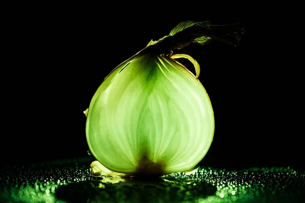 Rebanada de cebolla cruda con gotas de agua y luz de fondo verde neón sobre fondo negro - foto de stock