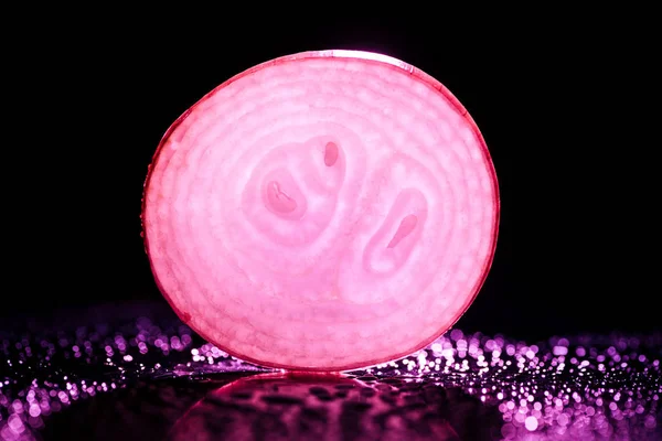 Fetta di cipolla cruda con gocce d'acqua e retroilluminazione rosa fluo su fondo nero — Foto stock