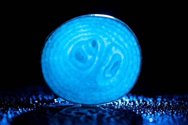 Slice of raw onion with water drops and neon blue back light on black background — Stock Photo