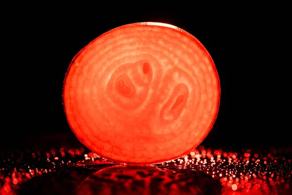 Slice of raw onion with water drops and neon red back light on black background — Stock Photo