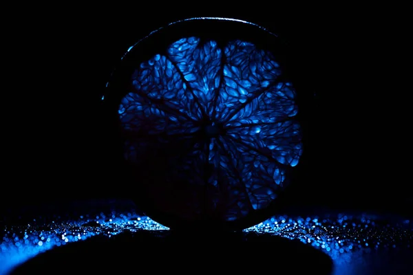 Slice of orange with neon blue backlit on black background — Stock Photo