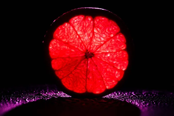 Rebanada de pomelo con neón rojo retroiluminado sobre fondo negro - foto de stock