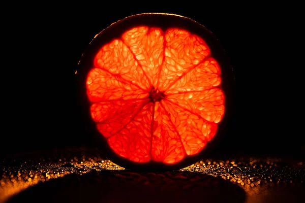 Slice of grapefruit with neon red backlit on black background — Stock Photo