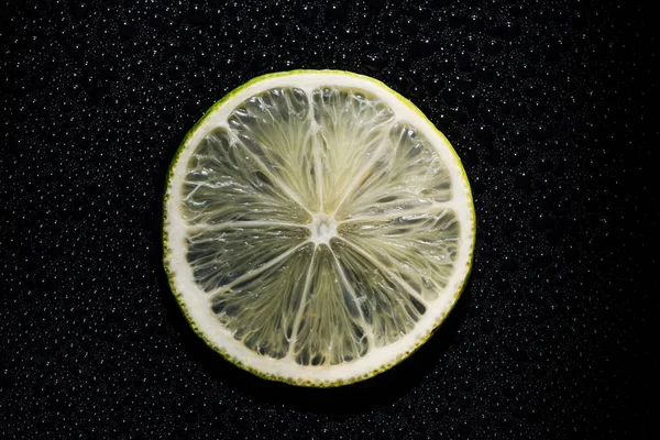 Slice of fresh lime on black background with water drops — Stock Photo