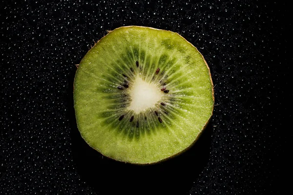 Slice of fresh kiwi fruit on black background with water drops — Stock Photo