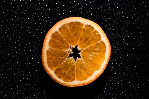 Slice of orange on black background with water drops — Stock Photo