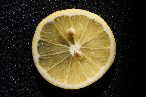 Fetta di limone fresco su fondo nero con gocce d'acqua — Foto stock