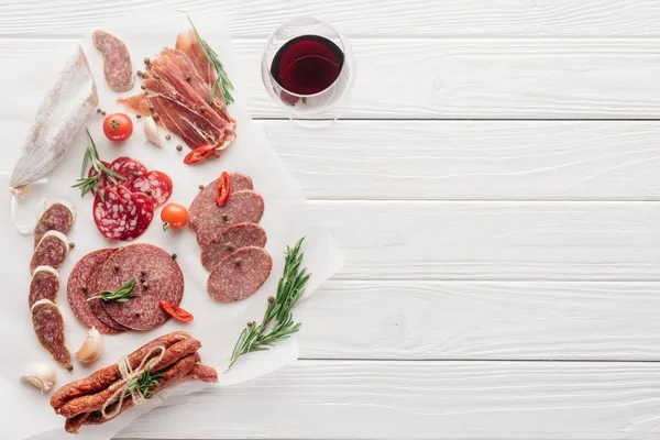 Composition alimentaire avec verre de vin rouge et collations de viande assorties sur plateau en bois blanc — Photo de stock