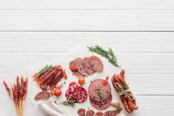 Top view of arrangement of various meat snacks and rosemary on white wooden backdrop — Stock Photo