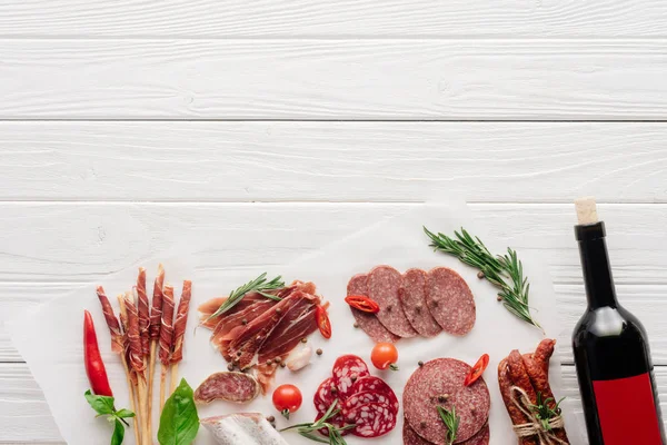 Posa piatta con spuntini di carne e bottiglia di vino rosso su sfondo di legno bianco — Foto stock