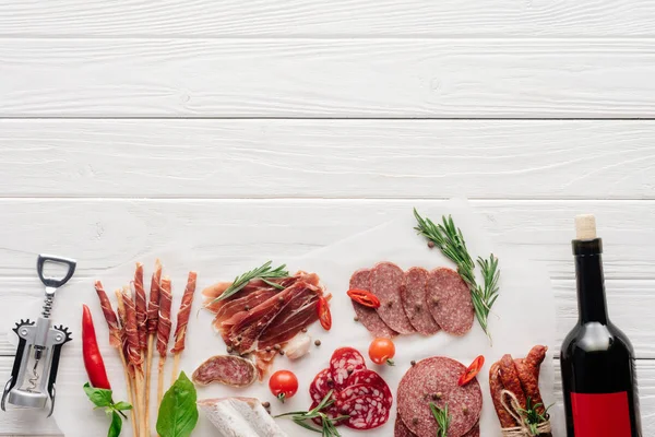 Acostado plano con botella de vino tinto, abrebotellas y aperitivos de carne en la superficie de madera - foto de stock