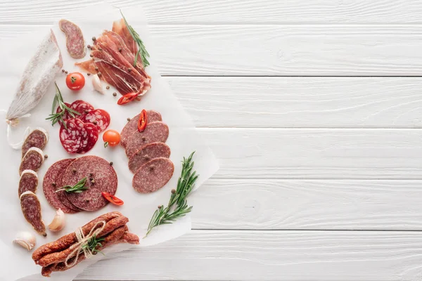 Draufsicht auf die Anordnung verschiedener Fleischsnacks und Rosmarin auf weißem Holzhintergrund — Stockfoto