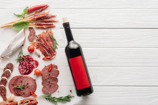Vista dall'alto di bottiglia di vino rosso e snack di carne assortiti su un tavolo di legno bianco — Foto stock