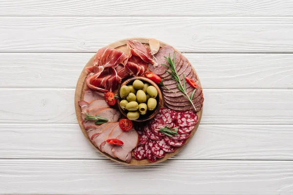 Vista superior de la disposición de varios bocadillos de carne y aceitunas sobre fondo de madera blanca - foto de stock