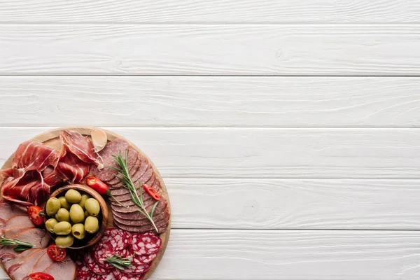 Top view of arrangement of various meat snacks and olives on white wooden backdrop — Stock Photo