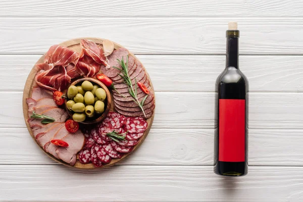 Vista superior de garrafa de vinho tinto e lanches de carne variados em mesa de madeira branca — Fotografia de Stock