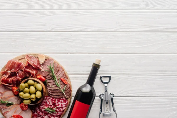 Flat lay com garrafa de vinho tinto, abridor de garrafas e lanches de carne na superfície de madeira — Fotografia de Stock