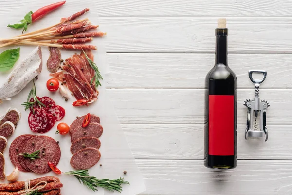Flat lay with bottle of red wine, bottle opener and meat snacks on wooden surface — Stock Photo