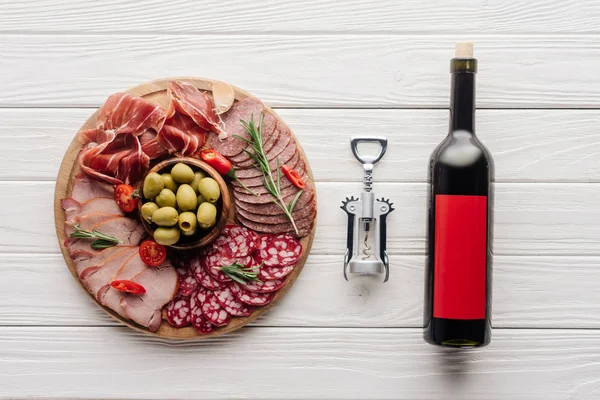 Flat lay com garrafa de vinho tinto, abridor de garrafas e lanches de carne na superfície de madeira — Fotografia de Stock