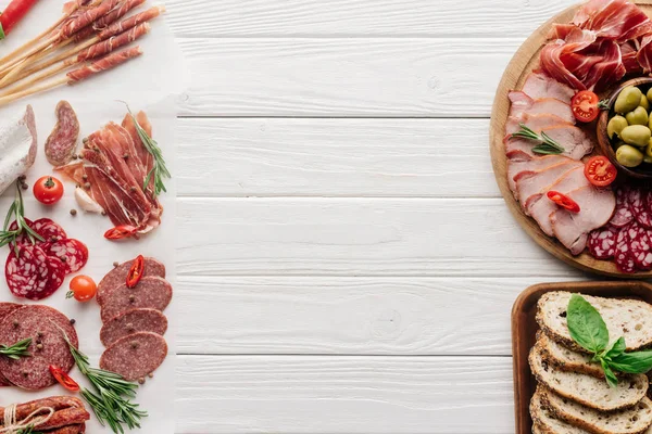 Draufsicht auf die Anordnung verschiedener Fleischsnacks und Oliven auf weißem Holzhintergrund — Stockfoto