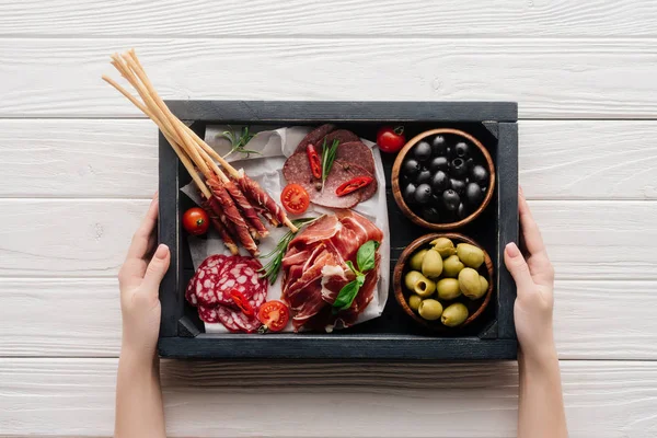 Cropped shot of woman holding box with different meat appetizers on white wooden surface — Stock Photo