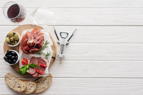 Flat lay with glass of red wine, pieces of bread and assorted meat snacks on white wooden tabletop — Stock Photo