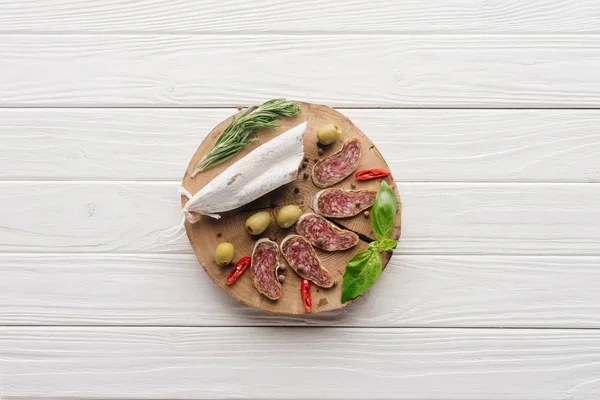 Vue de dessus des entrées de viande aux olives, au romarin et aux feuilles de basilic sur plateau en bois blanc — Photo de stock