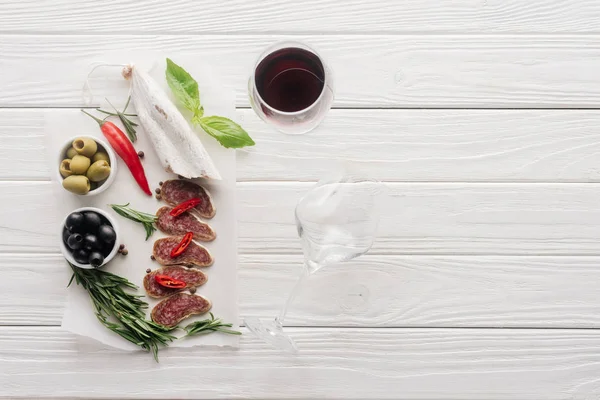 Composición de alimentos con copa de vino tinto y aperitivos variados de carne en la mesa de madera blanca - foto de stock