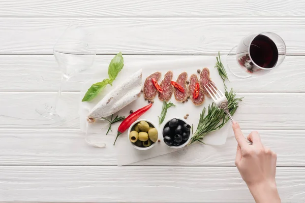 Colpo ritagliato di donna, bicchiere di vino rosso e spuntini di carne su superficie di legno bianca — Foto stock