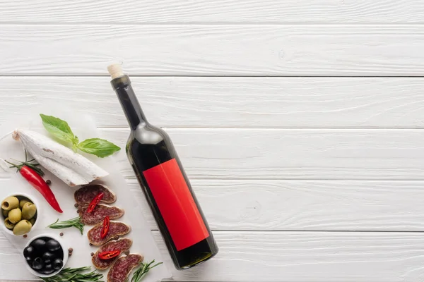 Top view of bottle of red wine and assorted meat snacks on white wooden tabletop — Stock Photo