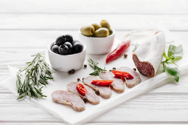 Vue rapprochée des entrées de viande aux olives, au romarin et aux feuilles de basilic sur plateau en bois blanc — Photo de stock