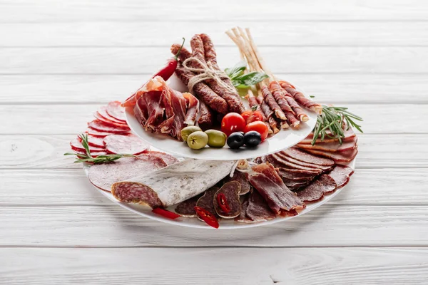 Закрытый вид на вкусные мясные закуски с оливками и розмарином на белом деревянном столе — стоковое фото