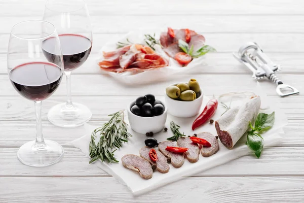 Nahsicht auf leckere Fleischvorspeisen und Rotweingläser auf weißer Holzoberfläche — Stockfoto
