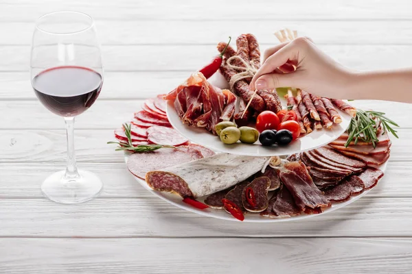 Colpo ritagliato di donna, bicchiere di vino rosso e spuntini di carne su superficie di legno bianca — Foto stock
