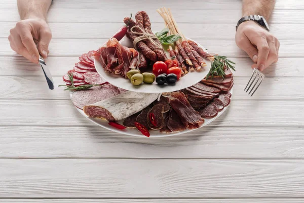 Partial view of man with cutlery at white wooden tabletop with various meat snacks — Stock Photo