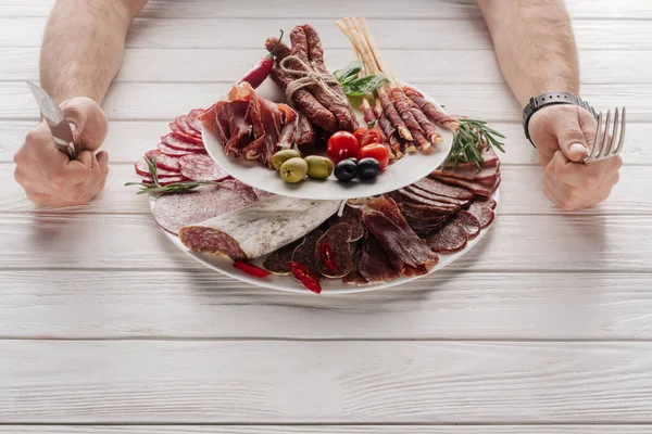 Partial view of man with cutlery at white wooden tabletop with various meat snacks — Stock Photo