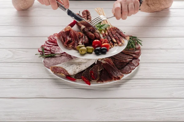 Vista parcial del hombre en la mesa de madera blanca con varios bocadillos de carne - foto de stock