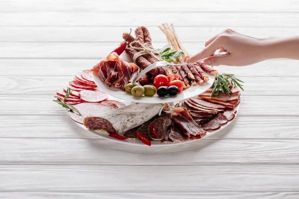 Tiro recortado de mujer probando diferentes aperitivos de carne en la superficie de madera blanca - foto de stock