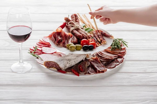 Cropped shot of woman, glass of red wine and meat snacks on white wooden surface — Stock Photo